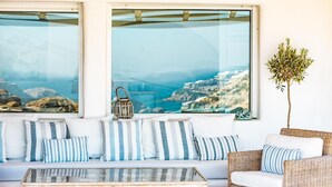 Un área de descanso con sofá y sillones, una mesa de centro de vidrio y vistas a un paisaje costero a través de grandes ventanales.