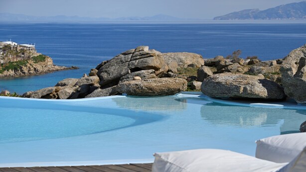 Una piscina con agua cristalina azul, rodeada de grandes rocas y una terraza de madera.
