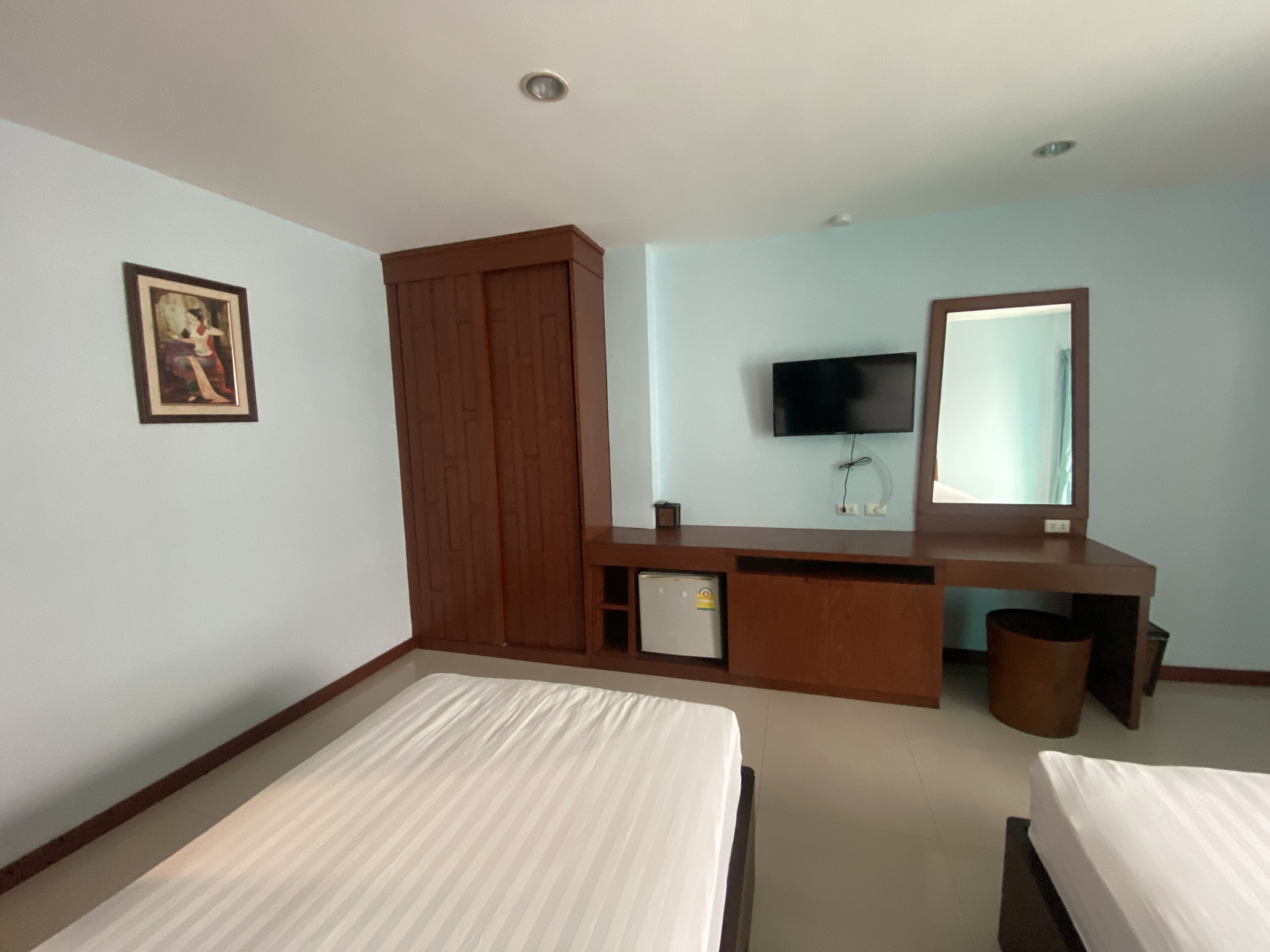 Habitación de hotel con dos camas individuales, un armario de madera, un escritorio con televisor y un espejo.