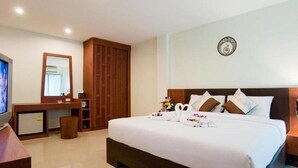 A hotel room with a large bed, a wooden desk, a television, and a mirror. - Cocoon Deva Hotel (Patong)
