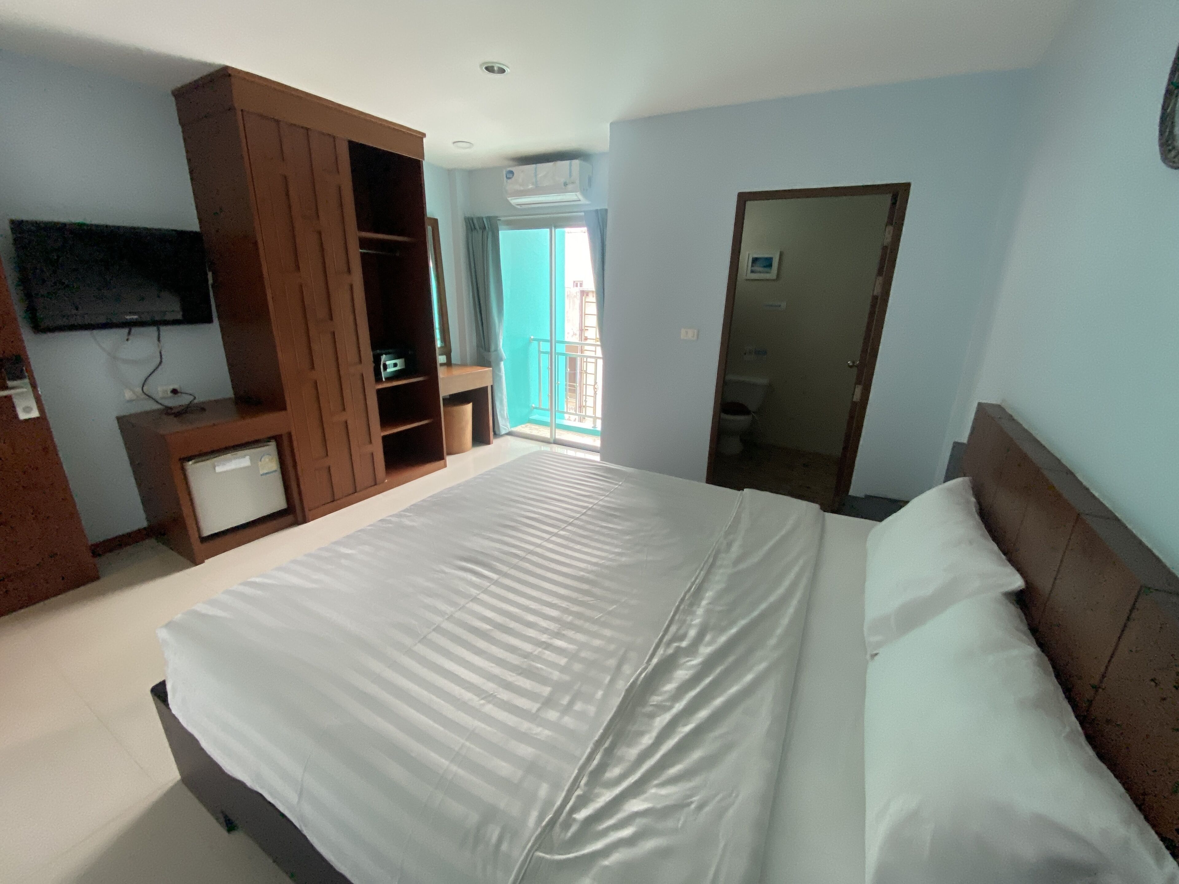 Ein Hotelzimmer mit einem großen Bett, einem Kleiderschrank, einem Fernseher und einem Balkon.