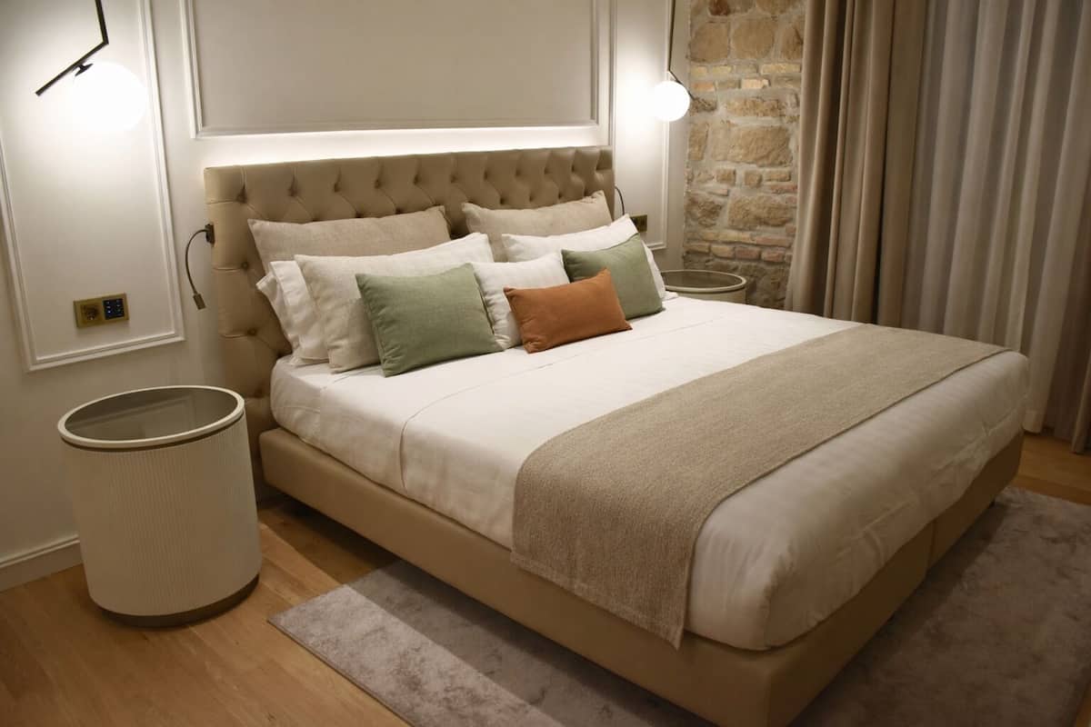 A neatly made bed with a tufted headboard, a bedside lamp, and a round trash bin.