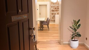 A hotel room with a wooden floor, a potted plant, a door labeled "Martina Suites," and a stone wall in the background. - Martina Suites (Rome)