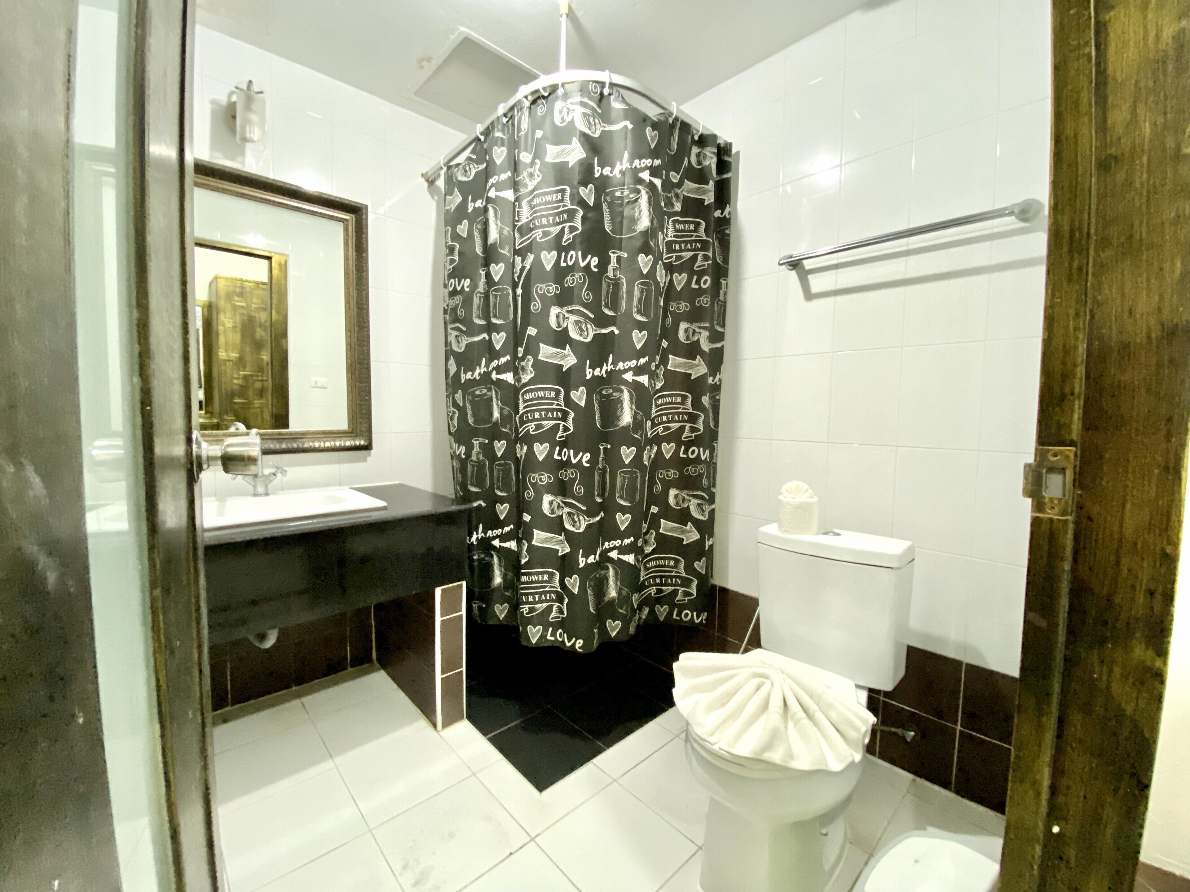 A bathroom with a shower curtain featuring bathroom-related doodles, a white toilet, and a mirror above the sink.