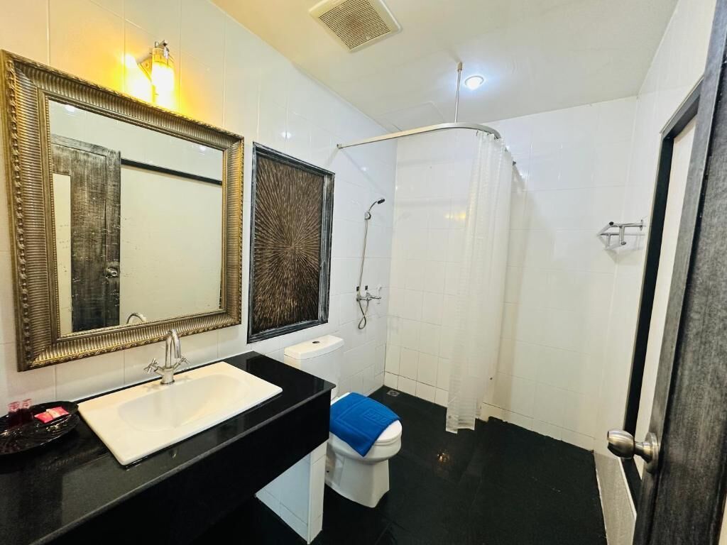 A bathroom with a black countertop, white sink, two mirrors, a shower curtain, and a toilet with a blue bath mat.