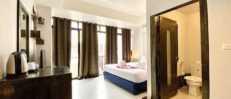 A hotel room with a bed, a desk, a mirror, and a view of the outside.