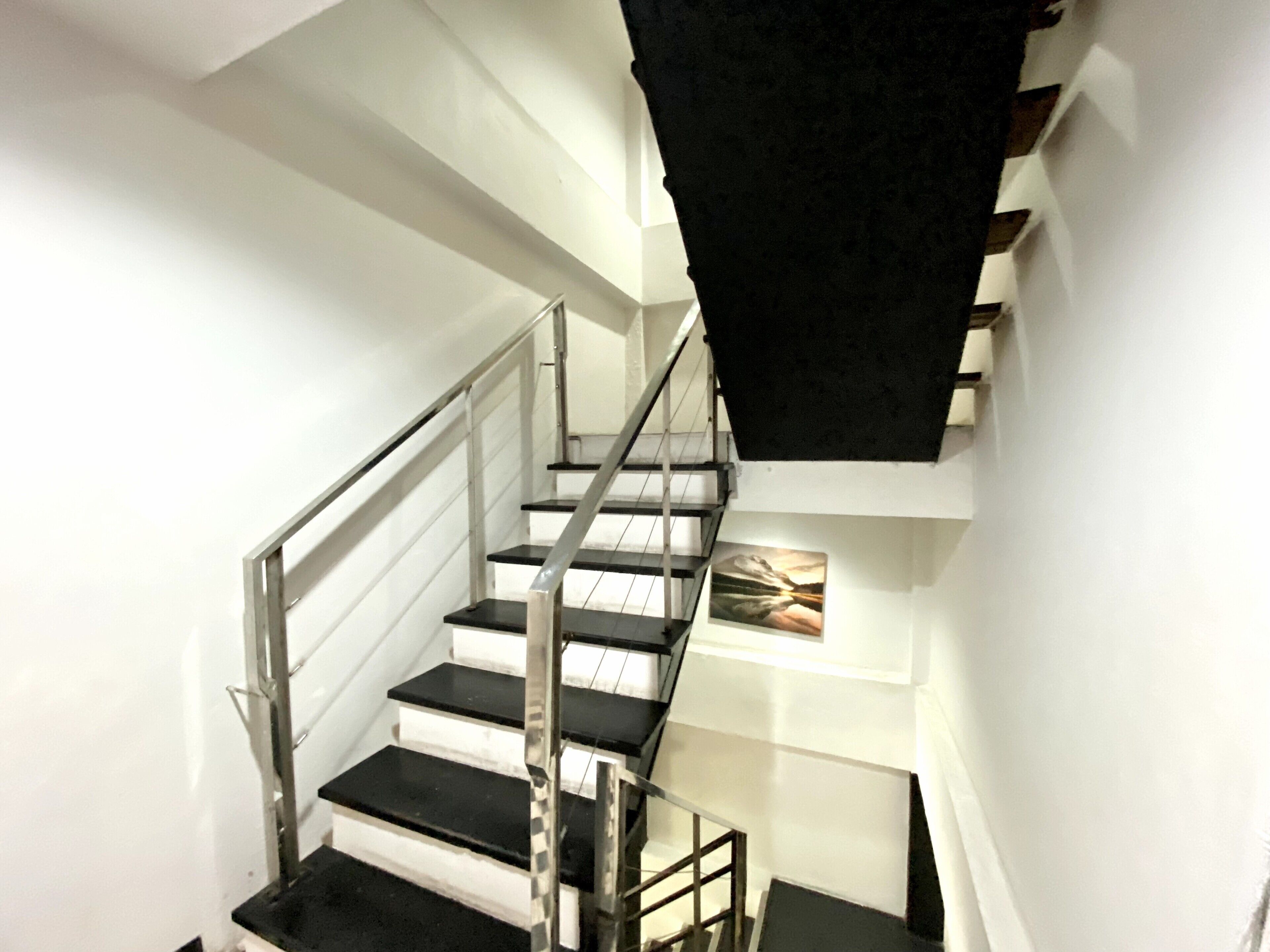 A modern staircase with black steps and metal railings, leading to a landing with a black cloth draped over the railing.