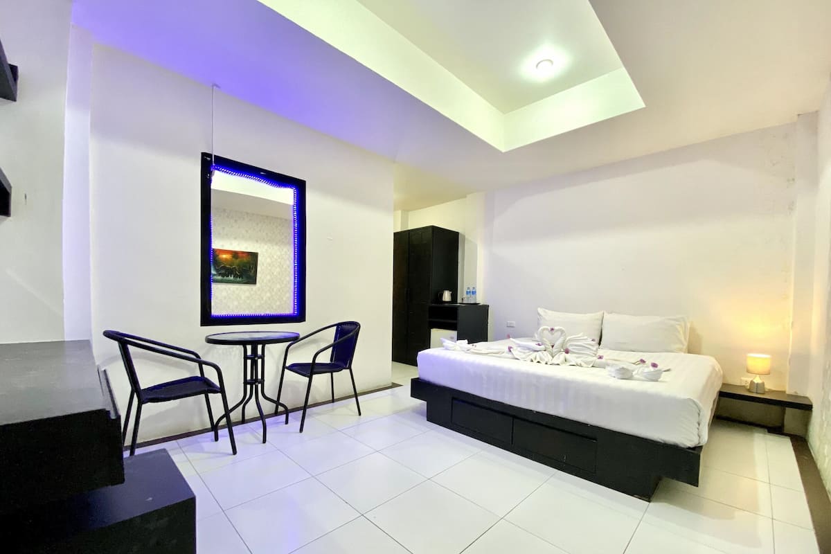 A modern hotel room with a bed, a desk, two chairs, a small table, and a mirror with LED lighting.