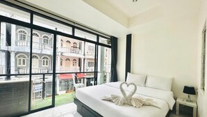A hotel room with a large bed, a nightstand, and a view of a building through large windows. - Beachwalk Patong (Patong)