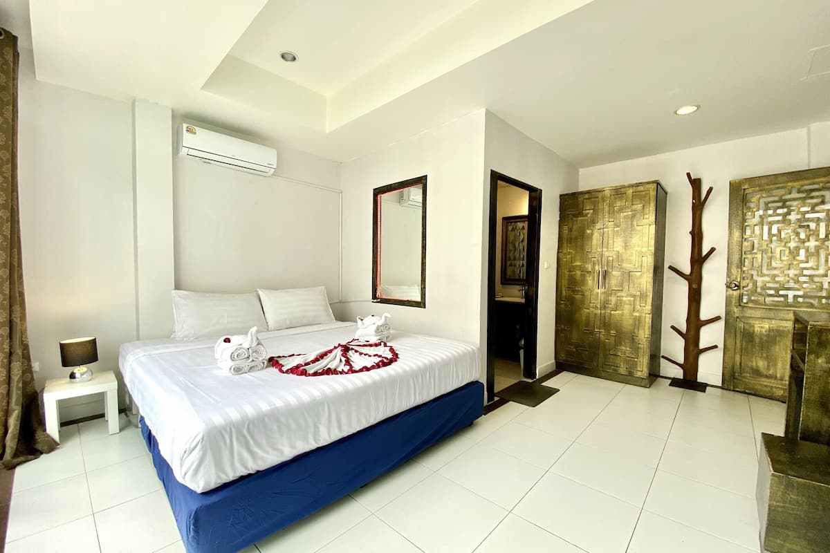 A hotel room with a bed, a nightstand, an air conditioner, a mirror, and a wardrobe.