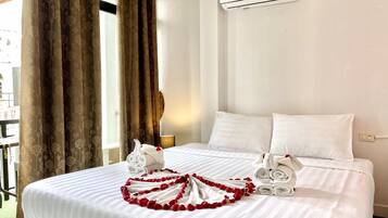Quarto de hotel com cama, roupa de cama branca, janela com cortinas, ar condicionado e vista para o exterior.