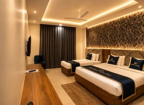 Ein Hotelzimmer mit zwei Betten, einem Schreibtisch, einem Stuhl, einem Deckenventilator und einem großen Fenster mit Vorhängen.