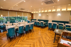 Een restaurant met een visgraatmotief houten vloer, teal bekleden stoelen en tafels met witte tafelkleden.