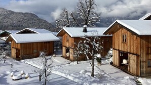 Une rangée de cabanes en bois aux toits enneigés, avec une chaîne de montagnes en arrière-plan.