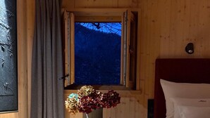 A wooden room with a bed, a window with curtains, a vase with flowers, and a rug. - Chalet am Quittenbaum, whole house, 140 sqm for 2-6 persons, 2 bedrooms, 2 bathrooms, sauna (Unterwössen)