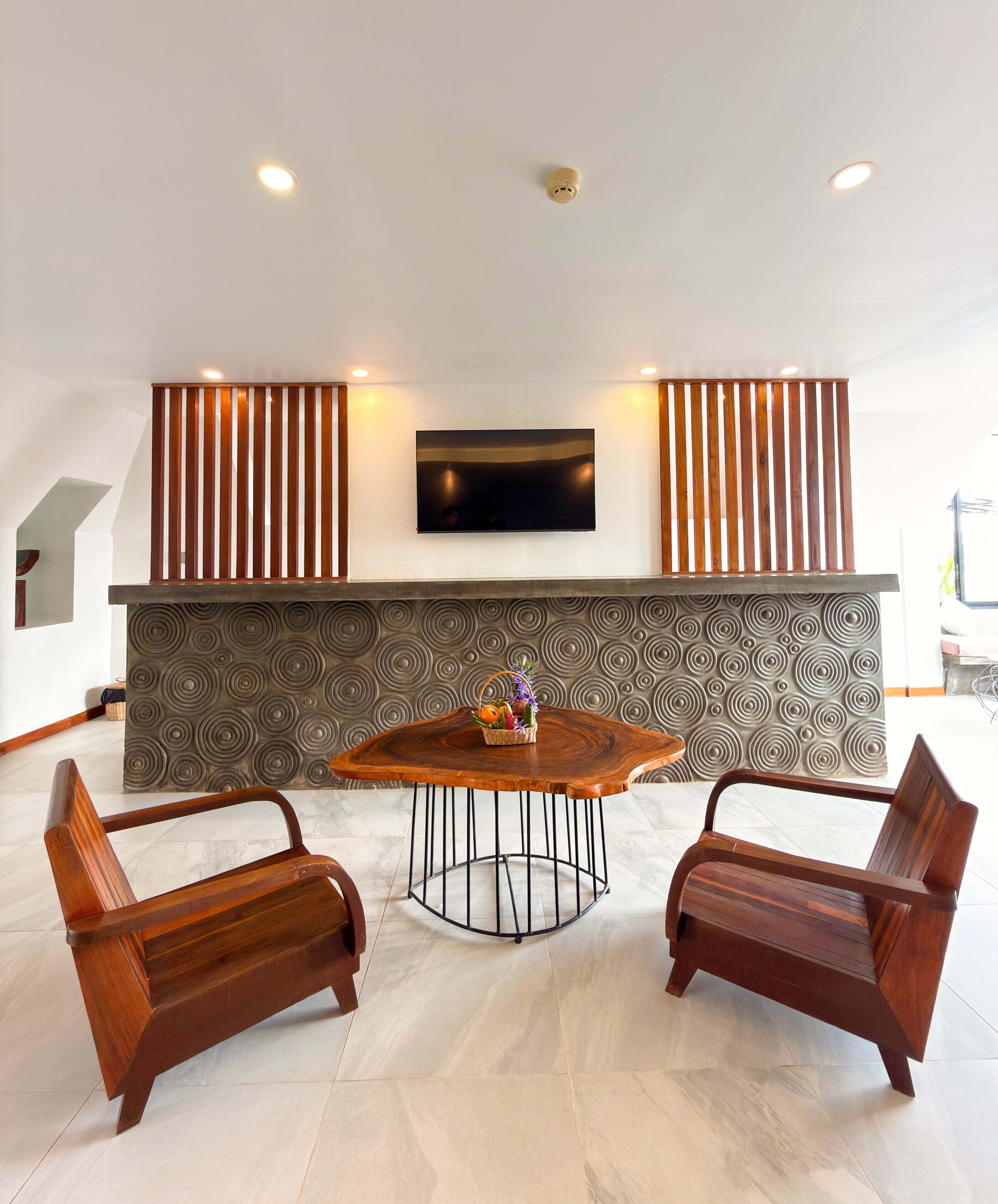 A modern interior with a round wooden table, two wooden chairs, a flat-screen TV mounted on the wall, and a patterned wall design.