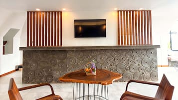 A modern interior with a round wooden table, two wooden chairs, a flat-screen TV mounted on the wall, and a patterned wall design.