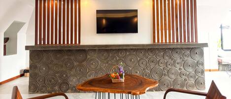 Un interior moderno con una mesa redonda de madera, dos sillas de madera, un televisor de pantalla plana montado en la pared y un diseño de pared con motivos.