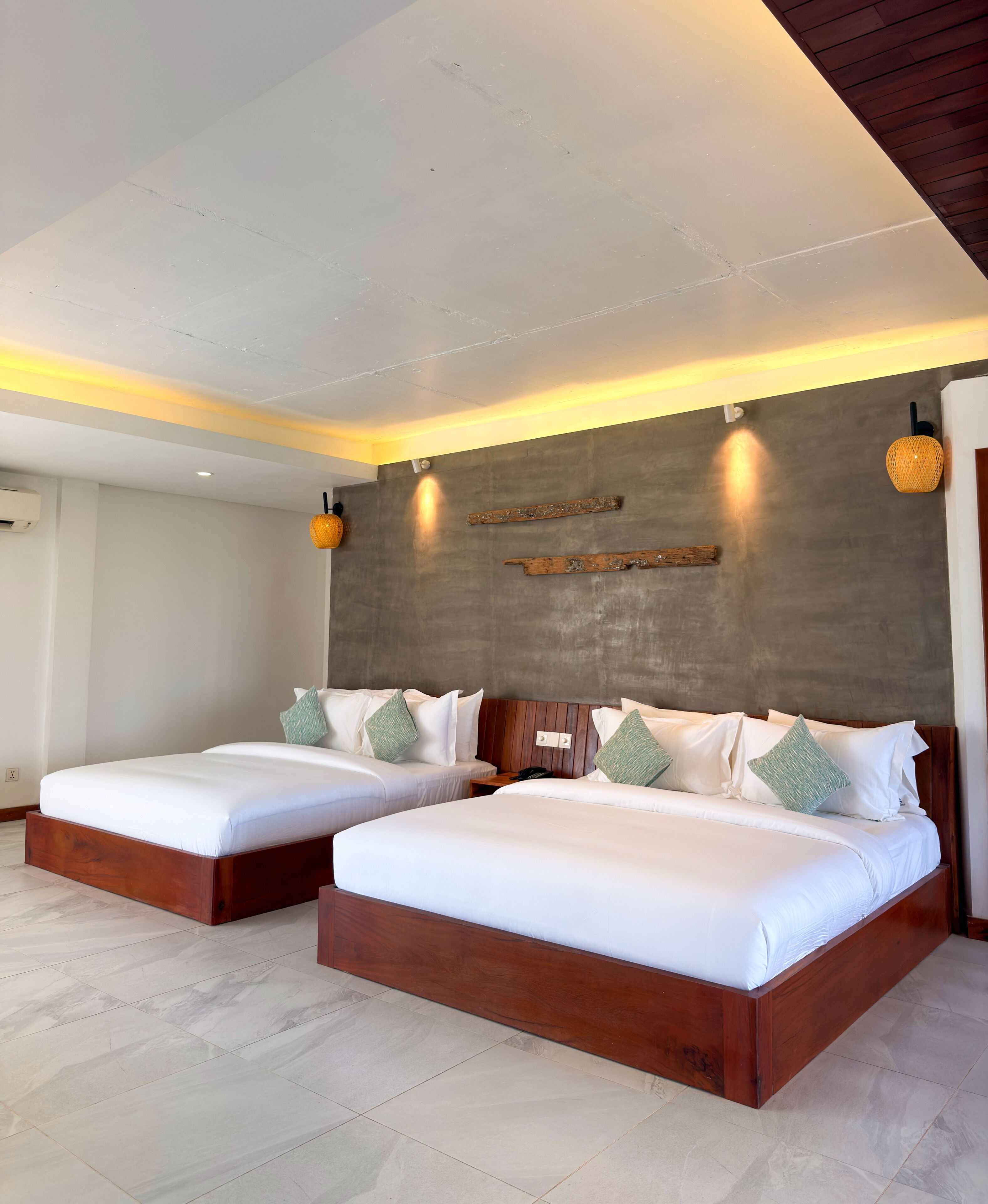 A hotel room with two beds, a wooden headboard, a wall-mounted light fixture, and a textured wall.