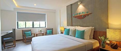 Une chambre d’hôtel avec un grand lit, un bureau, deux chaises, une fenêtre et une étagère fixée au mur, ornée d’objets décoratifs.