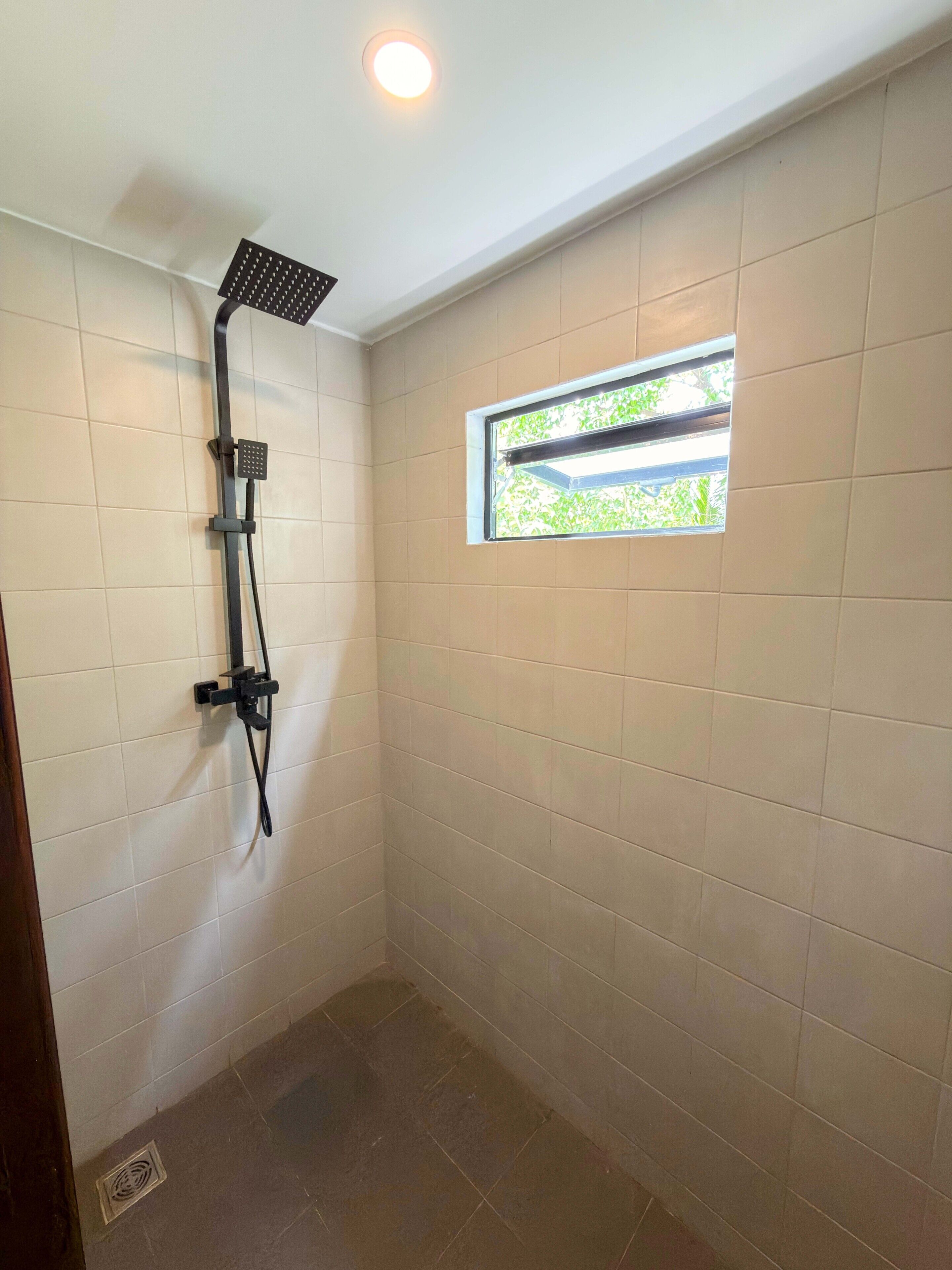 Ein kleines, gefliestes Duschbad mit Fenster und Deckenleuchte.