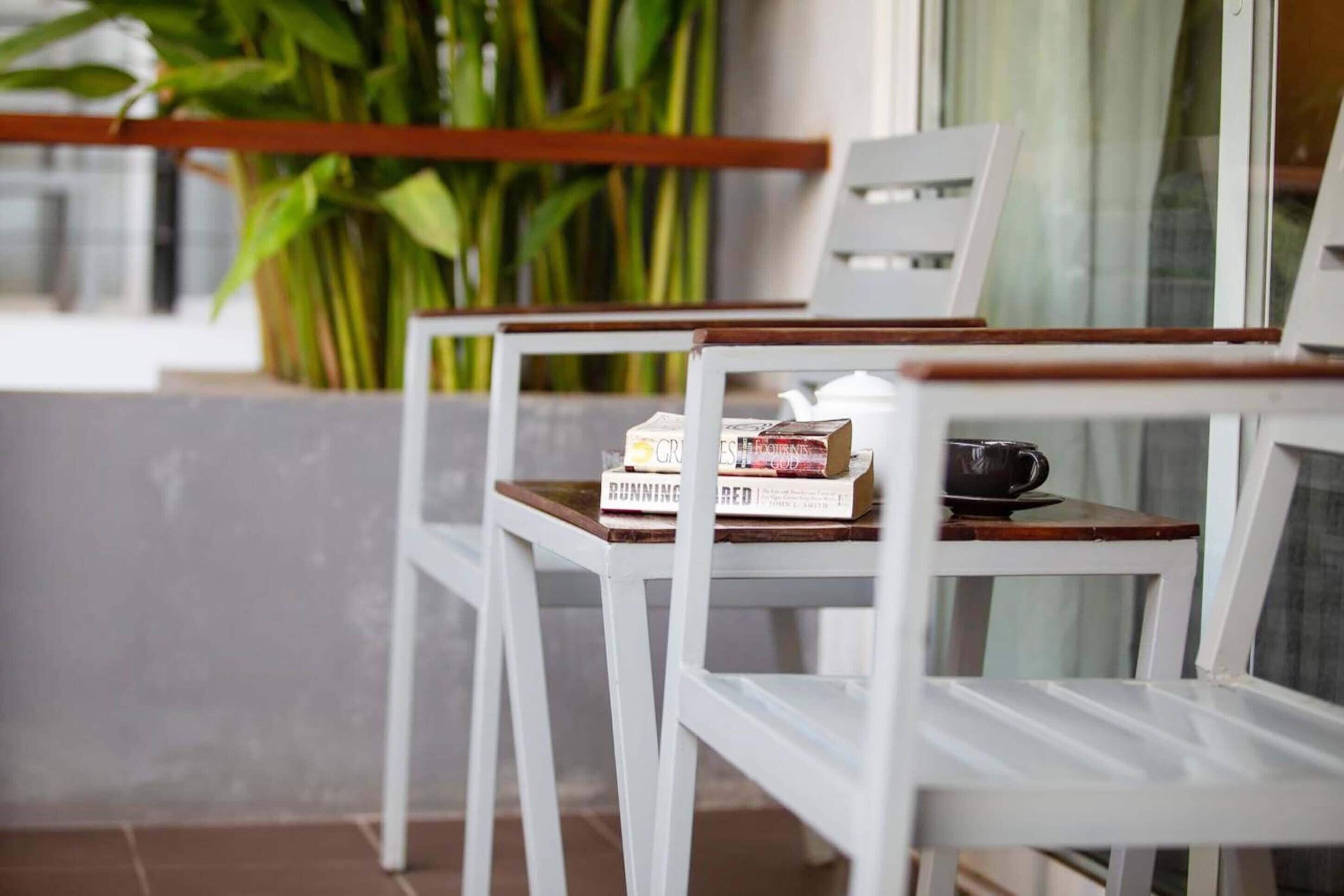 Duas cadeiras brancas com apoio de braço em madeira, uma mesa e um vaso com planta ao fundo.