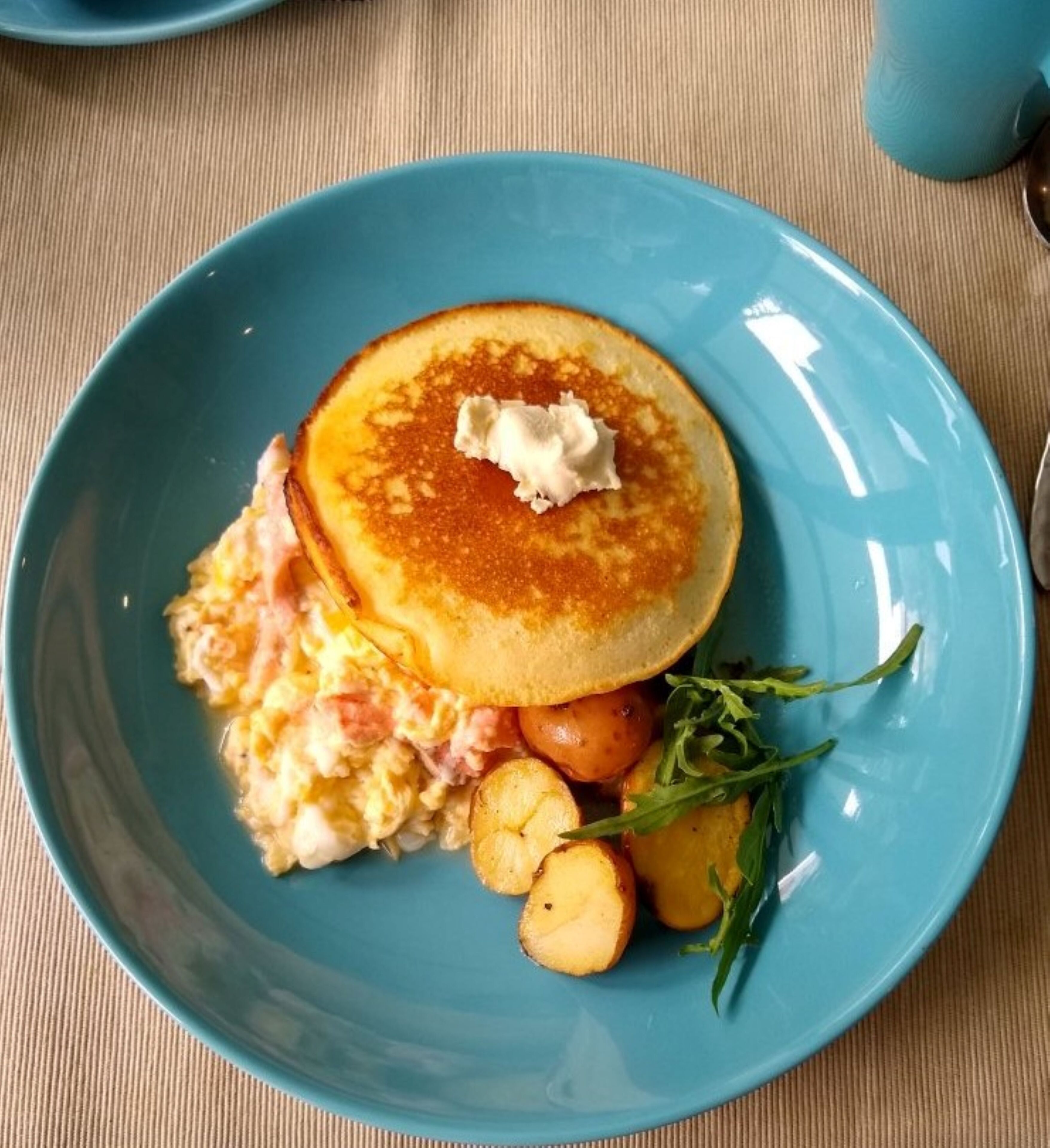 A plate with pancakes, scrambled eggs, roasted potatoes, and arugula.