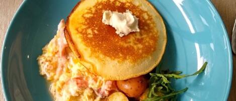 A plate with pancakes, scrambled eggs, roasted potatoes, and arugula.