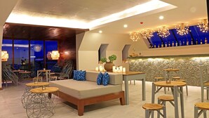 A modern lounge area with a sofa, round tables, and chairs, a bar with bottles, and a view of the night sky. - Riversoul Boutique (Siem Reap)