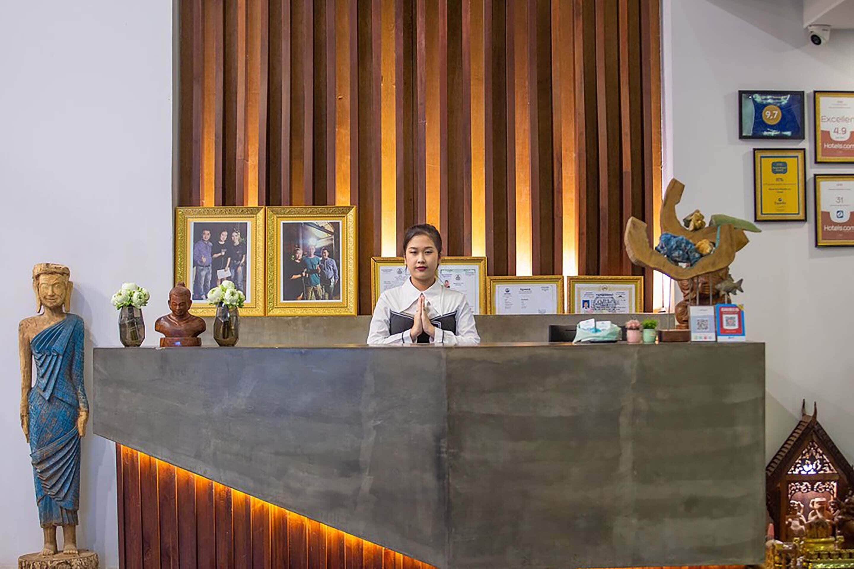 A reception desk with a wooden backdrop, framed pictures, and various decorative items including a Buddha statue and a small shrine.