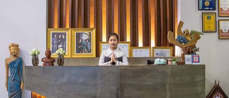 A reception desk with a wooden backdrop, framed pictures, and various decorative items including a Buddha statue and a small shrine.