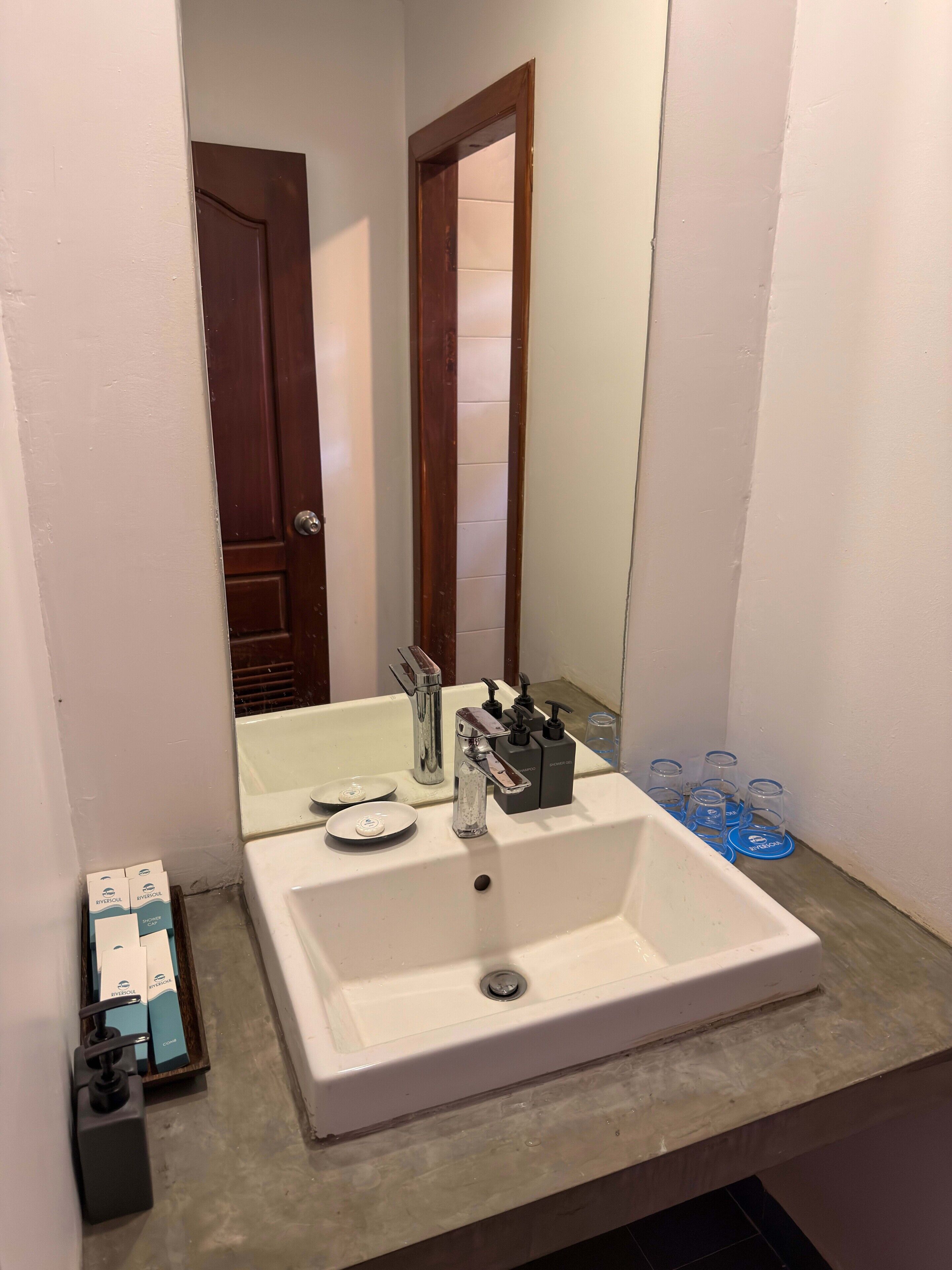 Un bagno con un lavandino bianco, uno specchio, una tenda della doccia e una porta.
