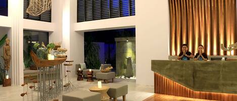 A modern lobby with a reception desk, seating area, and a large window with blinds.