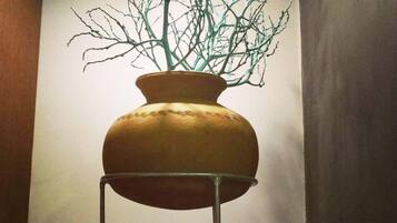 A ceramic vase with a branch-like structure inside, placed on a metal stand in a corner.