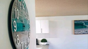 Un salon avec une horloge au mur, une petite table sur laquelle est posée une plante, et un fauteuil en osier.