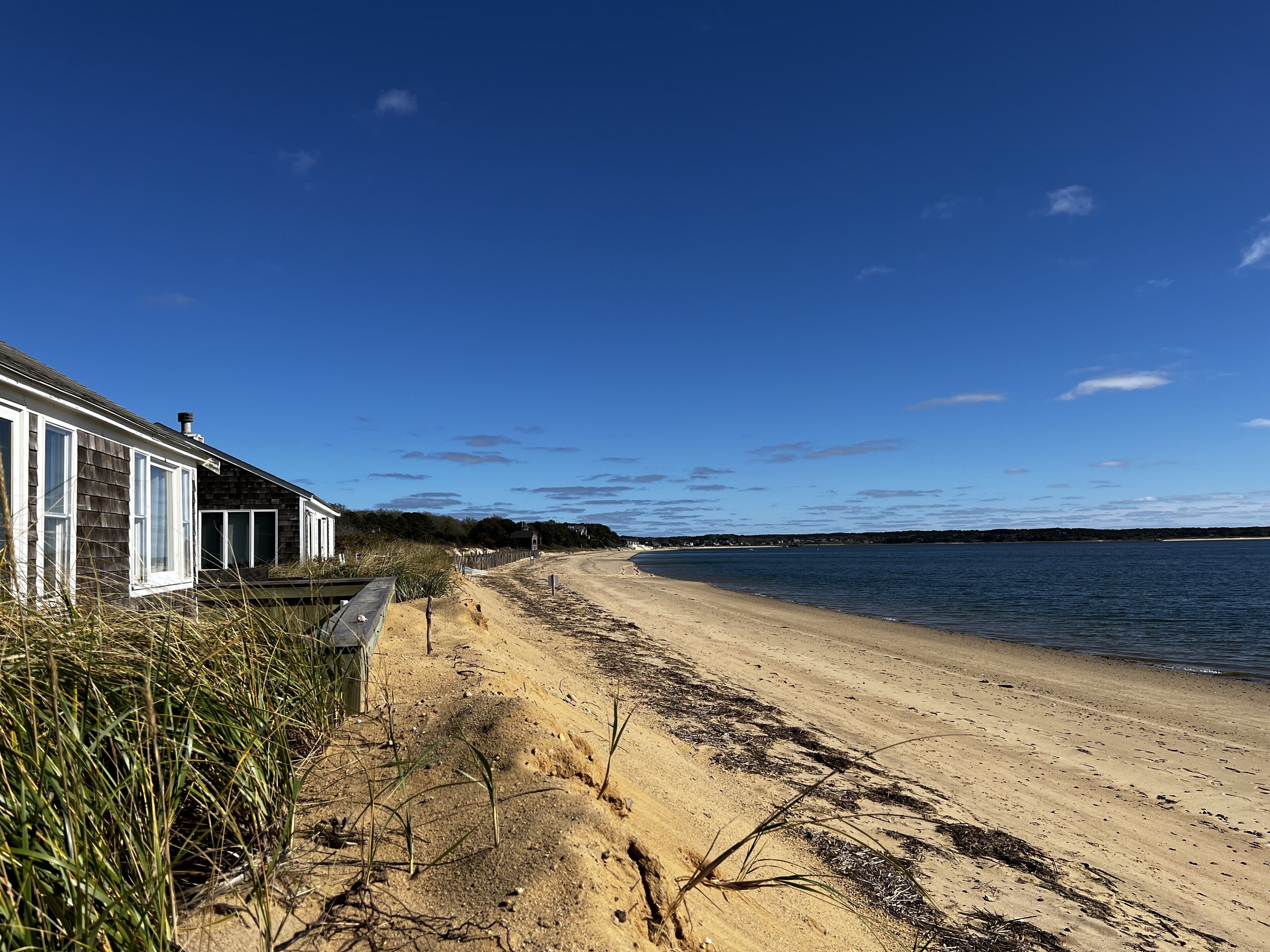 A sandy beach with a wooden house on the left, a clear blue sky, and a calm sea.