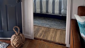 Een slaapkamer met een bed, een raam met gordijnen, een deur en een geweven mand op de vloer.