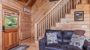 L’intérieur d’un chalet en bois, avec un canapé en cuir, un escalier en bois et une porte donnant sur l’extérieur.