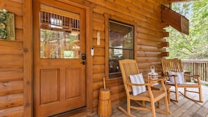 Une cabane en bois dotée d’un porche avec des fauteuils à bascule et une table.