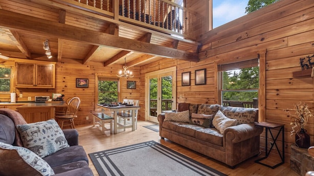 Un intérieur spacieux de chalet en bois, comprenant un coin repas, un ensemble de canapés et une cuisine.