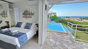 Un dormitorio con una cama grande, un baño con espejo y un balcón con vista a la piscina.