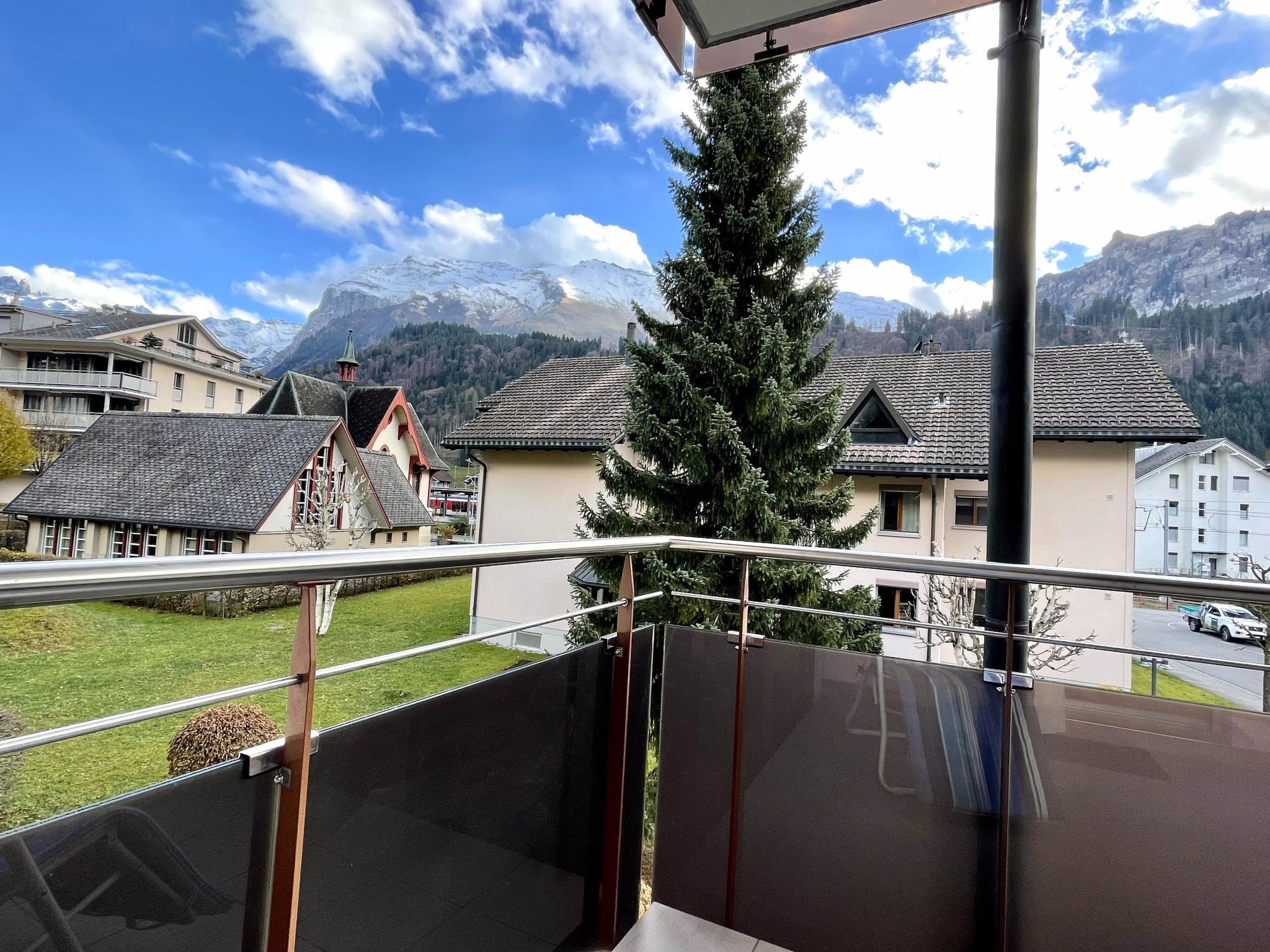 Un balcon offrant une vue sur une chaîne de montagnes, un arbre et un bâtiment doté d’un toit en pente.