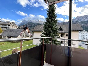 Un balcon offrant une vue sur une chaîne de montagnes, un arbre et un bâtiment doté d’un toit en pente.