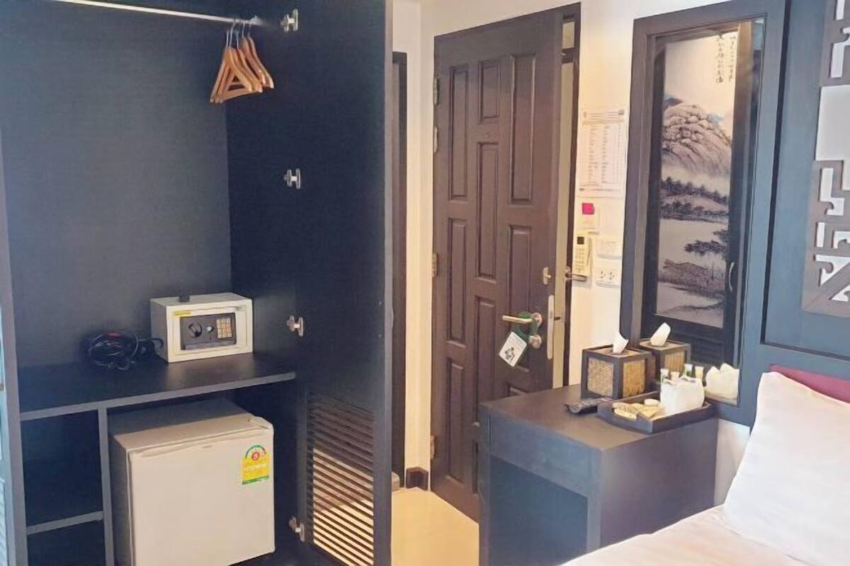 A hotel room with a bed, a desk with a computer, a small refrigerator, and a wardrobe.