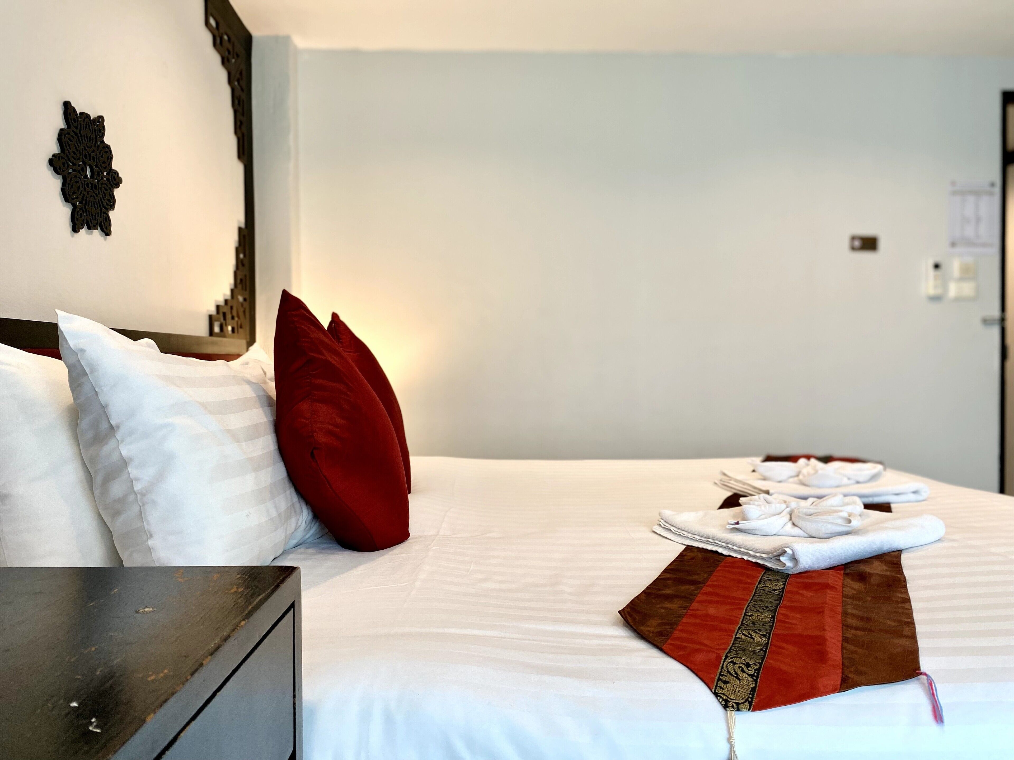 A neatly made bed with white and red pillows, a folded towel, and a decorative throw.