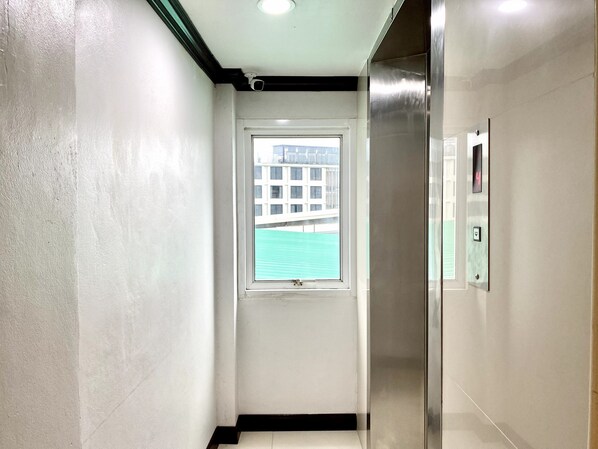 A narrow hallway with a door leading to a balcony with a view of buildings.
