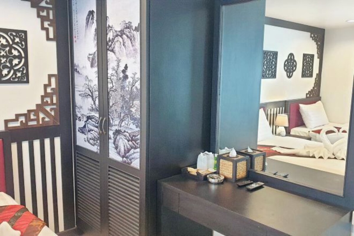 A hotel room with a traditional Chinese-style sliding door, a large mirror reflecting the bed, and a bedside table with amenities.