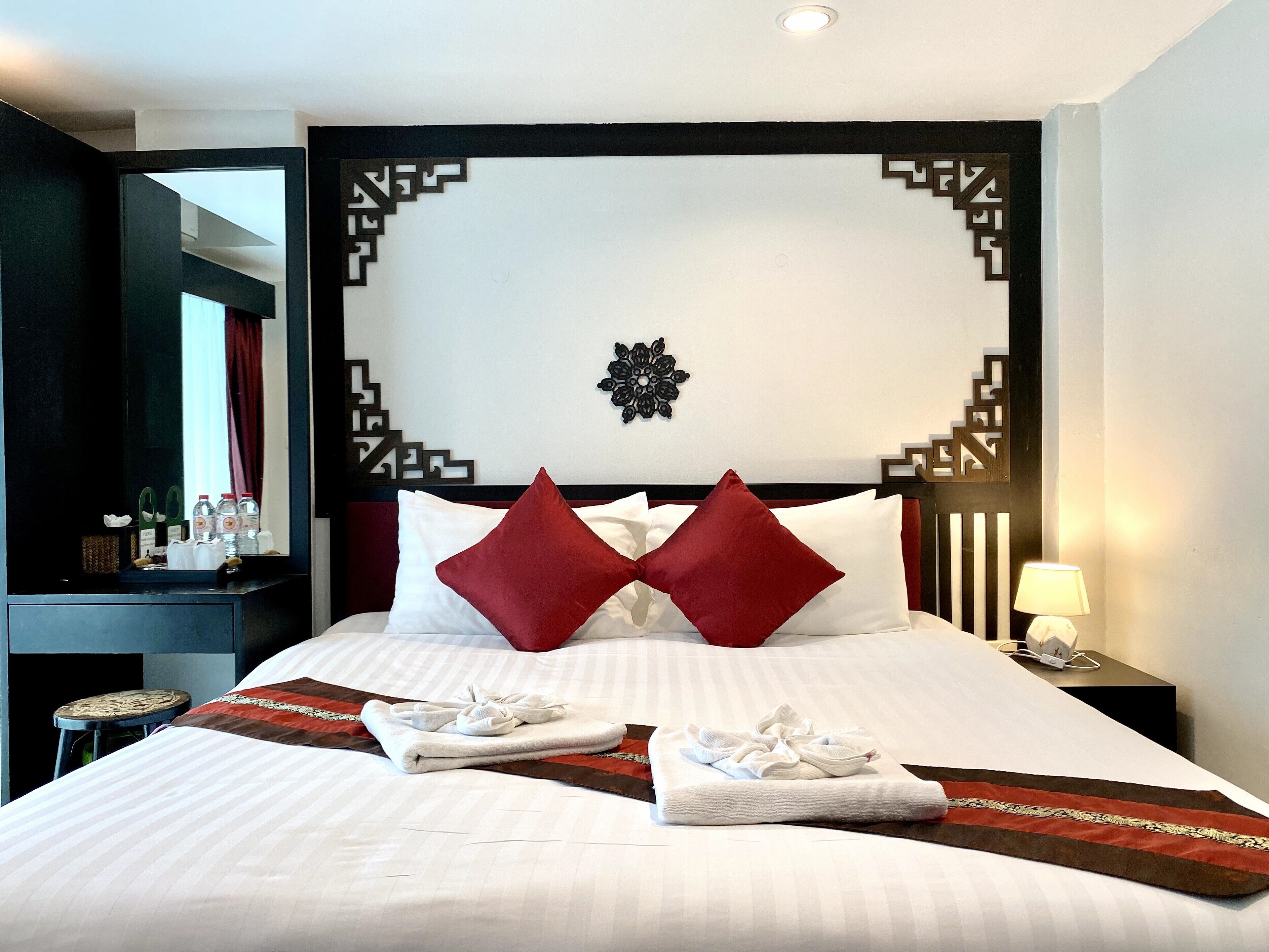 A hotel room with a neatly made bed, a decorative wall panel, and a small bedside table with a lamp.
