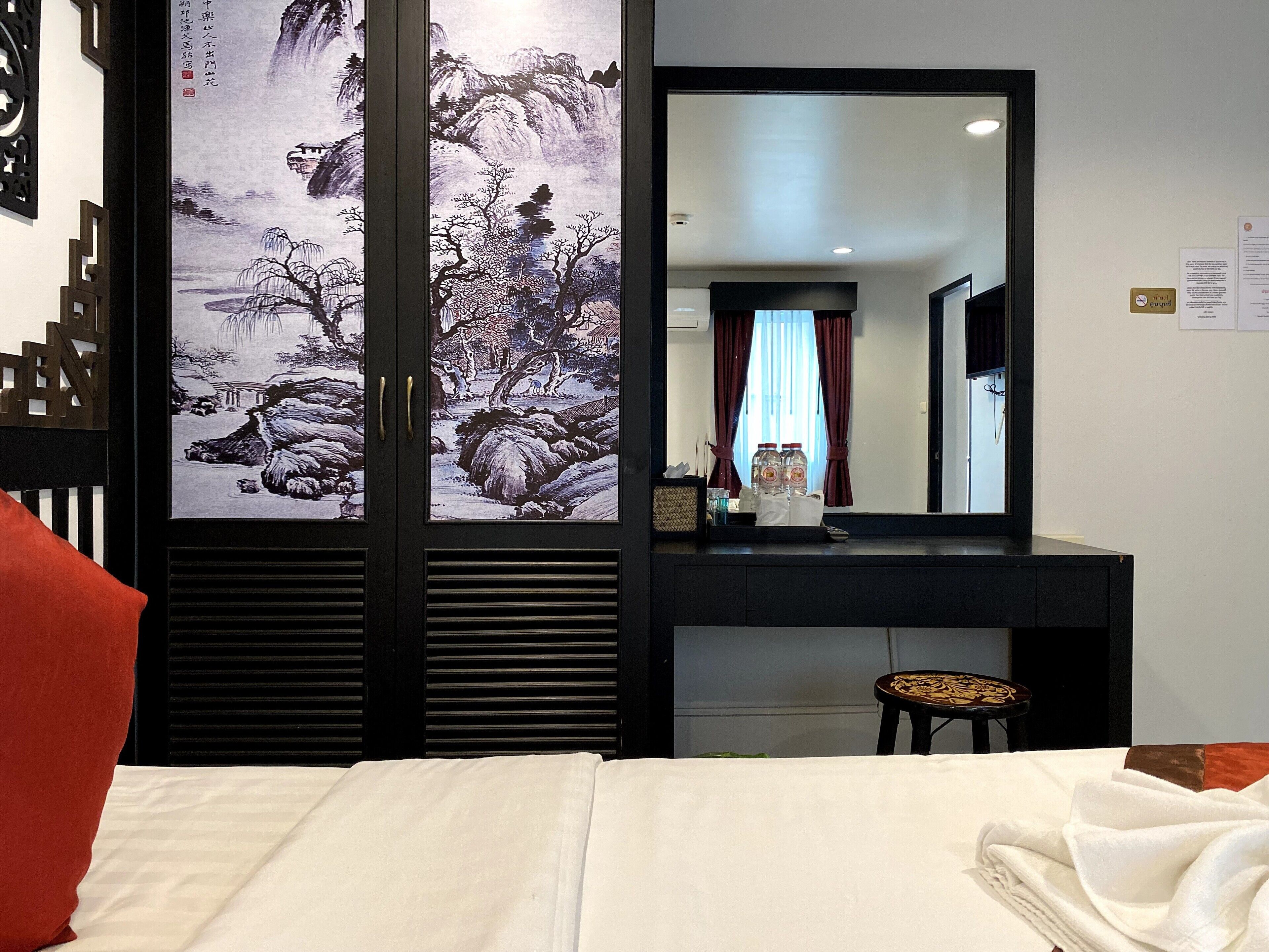 A hotel room with a bed, a dresser, a mirror, and a traditional Chinese painting on the wall.