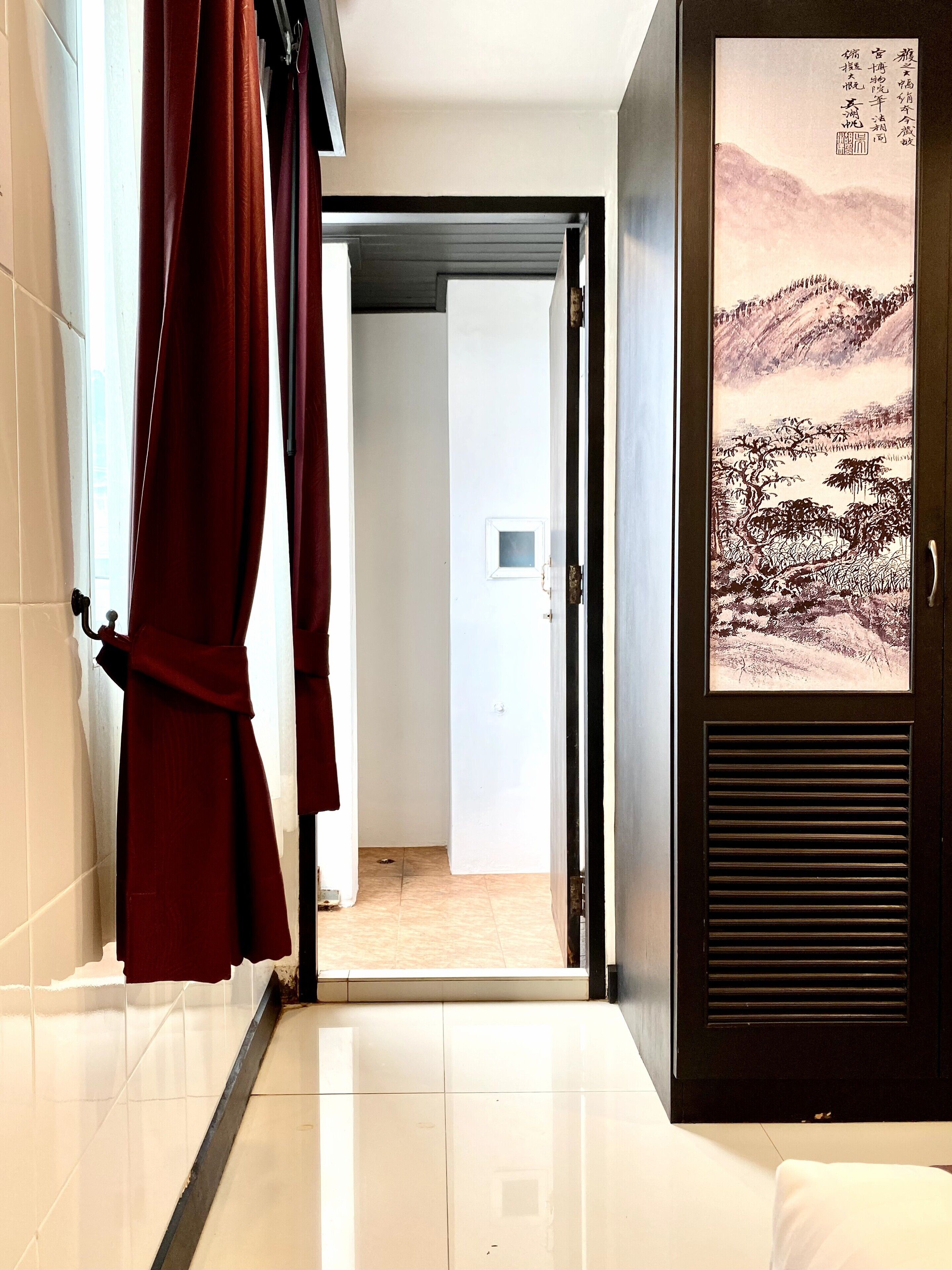 A hallway with a red curtain, a door leading to a room, and a wall with a framed artwork.